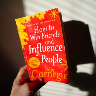 A hand holding the book How to Win Friends and Influence People by Dale Carnegie, a best book to read for self-development