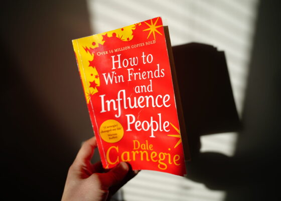 A hand holding the book How to Win Friends and Influence People by Dale Carnegie, a best book to read for self-development