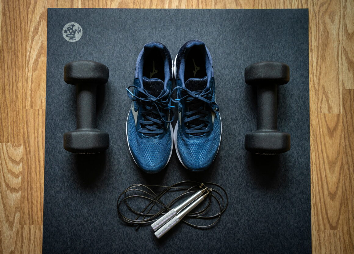 Workout equipment including running shoes, dumbbells, and jump rope as part of productive hobbies for active millennial men