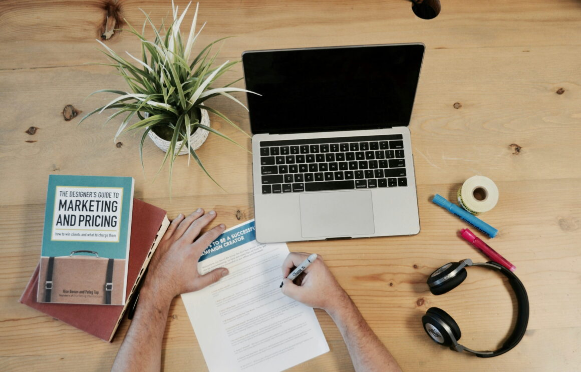 Workspace with laptop, marketing book, and notes on a wooden desk, representing research on does Amazon affiliate marketing still work in 2026.