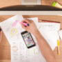 Person using a smartphone and highlighters while reviewing sketches and plans on paper in a home office, symbolizing strategic planning for Amazon affiliate marketing success in 2026.